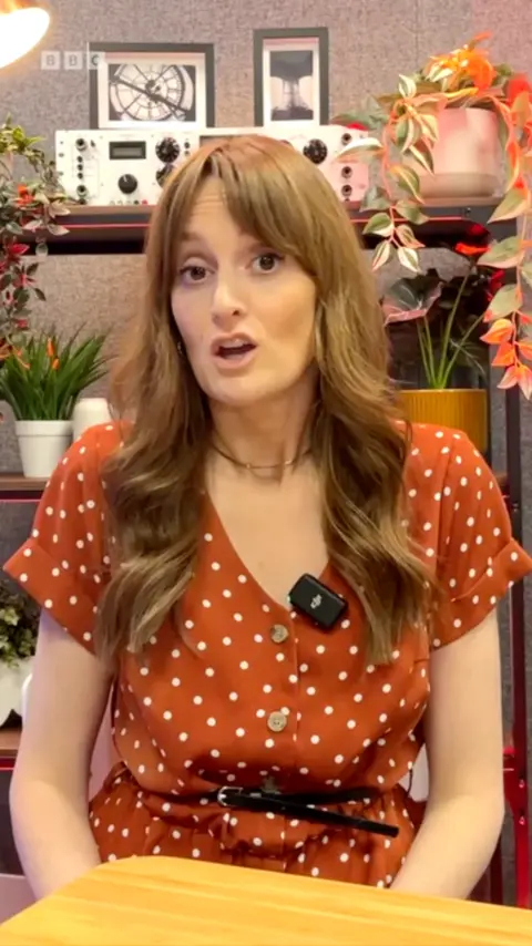 Harriet Robinson, a BBC journalist, sat at a table. She is looking into the camera.