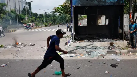 Reuters A demonstrator runs next to a vandalised police box during a protest demanding the stepping down of Bangladeshi Prime Minister Sheikh Hasina, following quota reform protests by students, in Dhaka, Bangladesh, August 4, 2024.