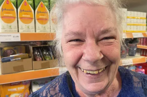 An elderly woman laughs in front of supermarket shelves