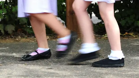 PA Media A picture showing the legs of two primary-school age girls in their uniforms