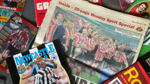 Michael Ganley A collection of old magazines and newspapers, mostly with Sunderland players on the front in red and white shirts. There is a Newcastle United programme in the left corner.