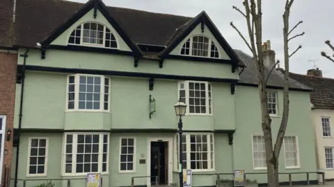 The exterior of Horsham Museum on Causeway, Horsham. The building is green with cream windows.