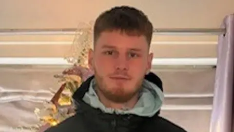 A close-up of Harvey Williams, an 18-year-old man wearing a black coat with a light green hood.