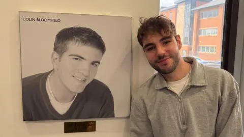 BBC Radio Derby producer Mitchell Barwell standing next to a photo of the late presenter Colin Bloomfield.