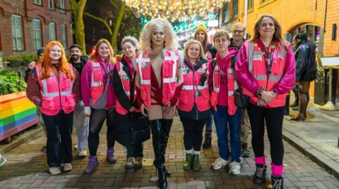 A group of volunteers are huddled together for a photograph. They are all wearing pink high-vis jackets. 