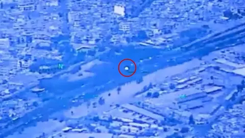 A white orb is circled with a red line soaring over a residential area. The image has a purple overlay.