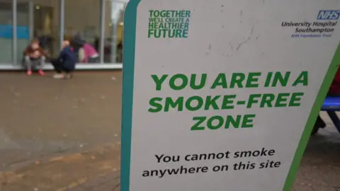 A sign saying you cannot smoke anywhere on this site with the hospital in the background
