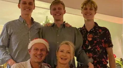 Family Handout A family photo of them together - three young men stand at the back with parents sitting in front, the middle-aged man wearing a santa hat.