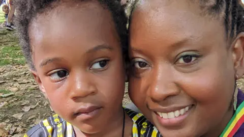 Bisi Daniels and her son Shaka, the shot is close to their faces as they sit together on the leafy ground in a park 