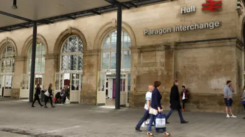 Exterior shot of Hull's Paragon Interchange. The stone building has large arched windows and a canopy. There are people walking along in the image.