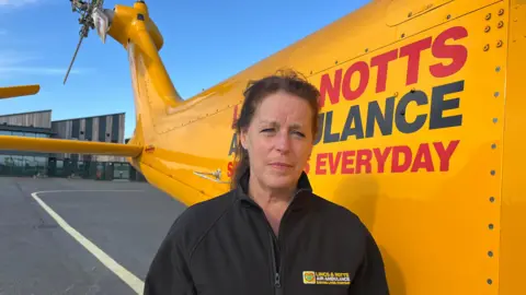 BBC/ALAN WEBBER A woman wearing a branded fleece stands in front of the LNAA ambulance.