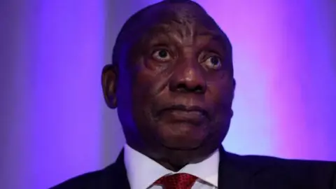 A close-up of President Cyril Ramaphosa wearing a black suit and a red tie 