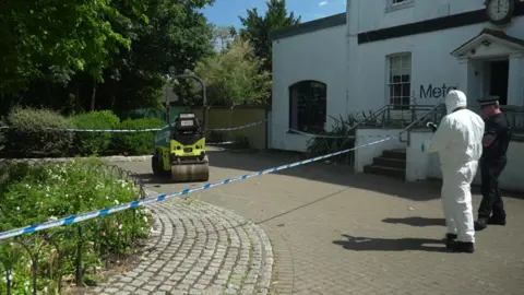 Jamie Niblock/BBC A small one-seater maintenance vehicle. It has one seat and a roller at the front. A forensics person in white overalls and a uniformed police officer are standing on the other side of police tape in front of it. There is a white building with the word "Meta" on its front.