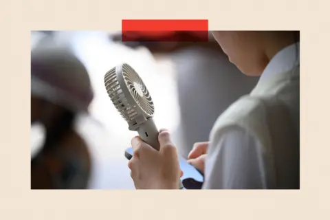 Bloomberg via Getty Images A person carries a handheld fan 

