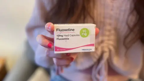 Lara is holding a box of fluoxetine antidepressants. 