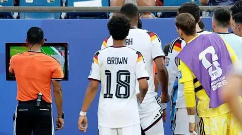 Germany players look on as referee Jalal Jayed watches a VAR replay 