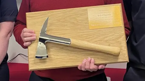 Office of Cumbria's Police, fire and crime commissioner A small axe that has been mounted to a wooden panel is being held up