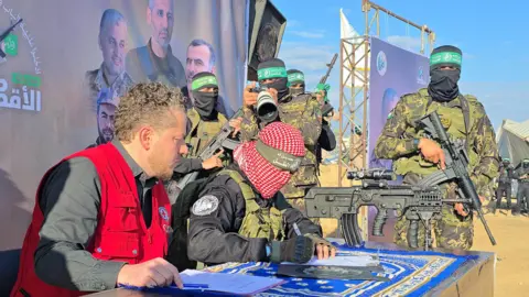 Getty Images A Hamas fighter and Red Cross official sign handover documents at a hostage release in Khan Younis, as other Hamas fighters look on.