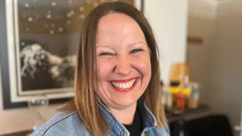 Woman with blone brown hair wearing red lipstick and denim jacket smiling at camera