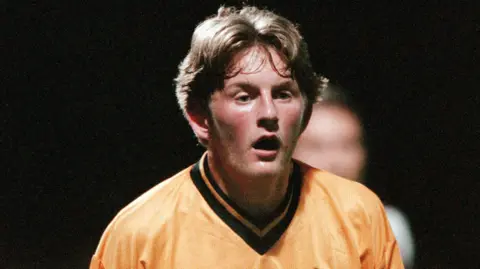 Getty Images Headshot image of Youngs who is standing on a football pitch. He has brown short hair and is wearing an orange football T-shirt which has a black neckline. 