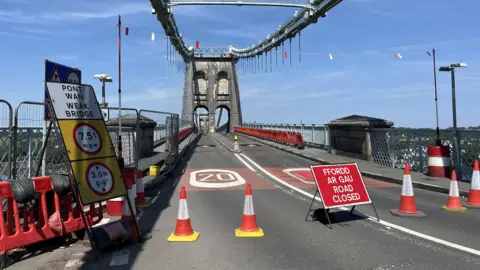 The bridge closed off by orange traffic cones and road closure signs on a sunny day. 