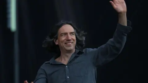 Getty Images Gary Lightbody smiling and waving. He is wearing a grey shirt