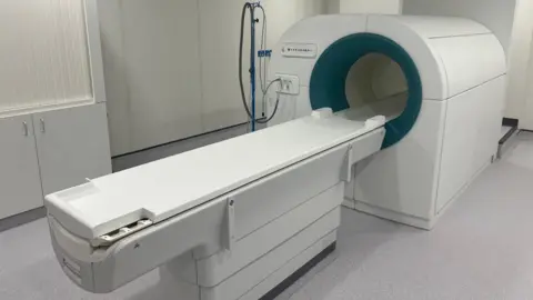 A hospital scanning machine with a bench for people to lie on which can move into the circular hole in front of the scanner.