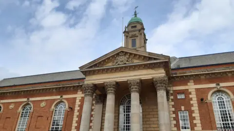 Local Democracy Reporting Service A close up of Peterborough Town Hall. It is a brown brick building with 4 pillars in front. A number of arched windows are also on the building.