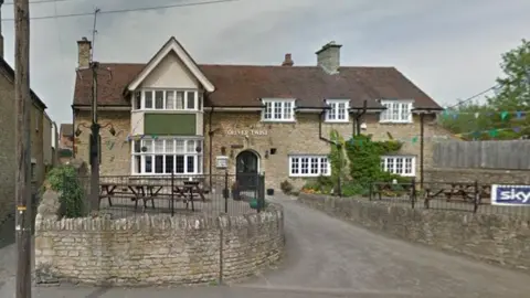 Google Two-storey pub building with bay window on both floors to the left and smaller windows to the right. There is a driveway to the entrance between two stone walls. "Oliver Twist" is spelt out in a sign above the door.