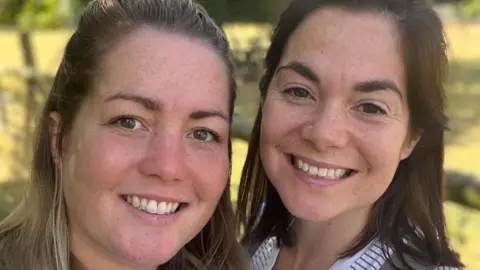 Two women in their thirties, Esme Sparks, who is blonde, and Lucy Sparks, who has dark hair. 