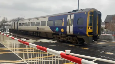 A two carriage Northern train is at a level crossing 