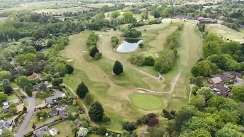 Qays Najm/BBC An aerial shot of a large golf course, which is surrounded by trees and residential properties.