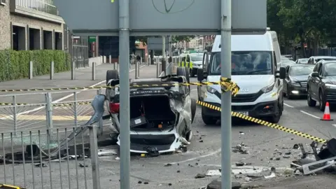 Leicester Media Online An overturned car at a city road junction, with cars and debris nearby