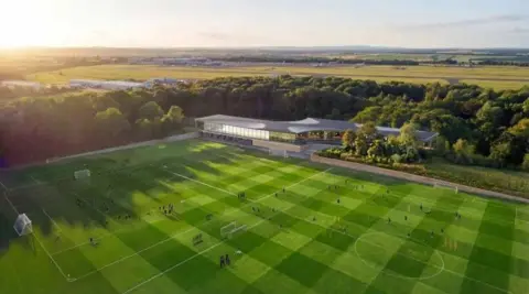 This artist’s impression shows a modern football training complex surrounded by green countryside. Several well-maintained pitches with players and training equipment fill the foreground, while a sleek, glass-fronted training building sits among trees in the centre. Beyond the facility are fields, woodland, and distant buildings, with warm sunlight creating a bright, peaceful atmosphere.