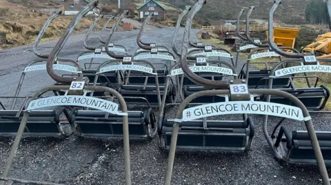 Glencoe Mountain ski chairs, the have the name on them and numbers and are lying on their backs along a stretch of road