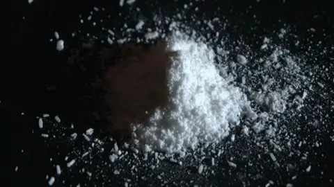 On a black table, a small pile of white powder lies. 