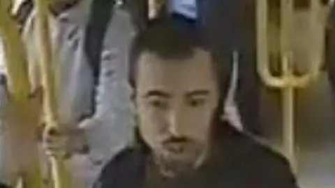 A picture lifted from CCTV of a man with short dark hair, a short dark beard and moustache, wearing a dark jacket.