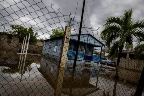 Getty Images A house is seen partially flooded behind a wire fence in the region of Guayama, Puerto Rico.