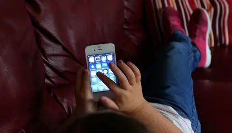 Small child sits on a sofa using a mobile phone.