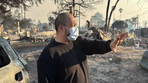 Larry Villescas berdiri di depan sisa-sisa lingkungannya yang hangus. 