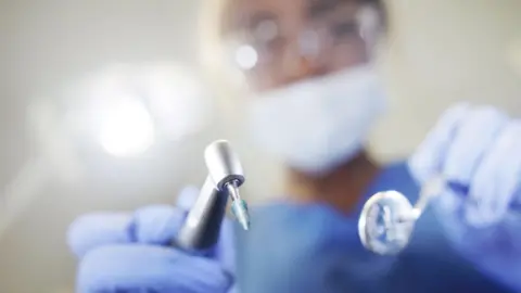 Getty Images A close up photo of a dentist holding tools. The identity is blurred.