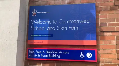 Red and blue sign for Commonweal School on a brick wall