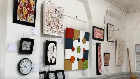 Luke Deal/BBC More pieces of The Hat's artwork hang on a white wall.