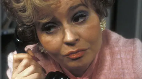 Prunella Scales in a pink top on the phone as Sybil in Fawlty Towers