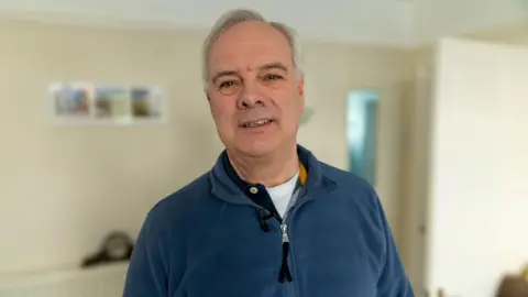 Ian Palmer/BBC Nick Evans, a historian who specialises in the history of Dreamland and other parts of Thanet, pictured in his home. He is wearing a blue fleece and has white hair.