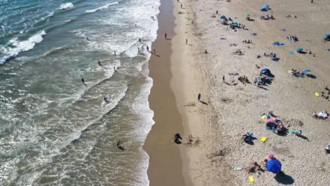 Getty Images A busy beach seen from a zoomed-out aerial shot, with people in the water and sitting on the sand with colourful umbrellas