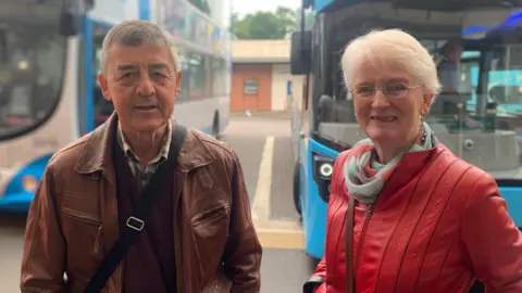 Brendan and Margaret Jamison - an older man with grey hair wears a brown leather jacket and a woman in a red leather jacket and white hair stands beside him