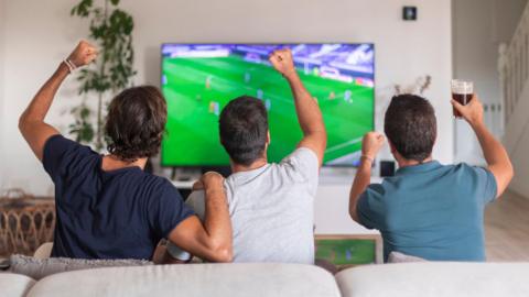Three men sitting on a sofa watching football on TV