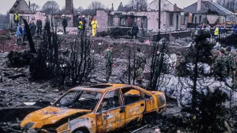 Getty Images Members of the armed forces collect debris from residential gardens after the mid-air explosion of Pan Am Flight 103 Clipper Maid of the Seas over Lockerbie, Scotland, UK, on Thursday, December 22, 1988. (Photo by Bryn Colton/Getty Images)