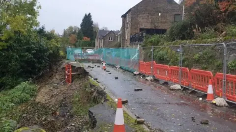 A road with a landslip on the near side with roadworks on the right
